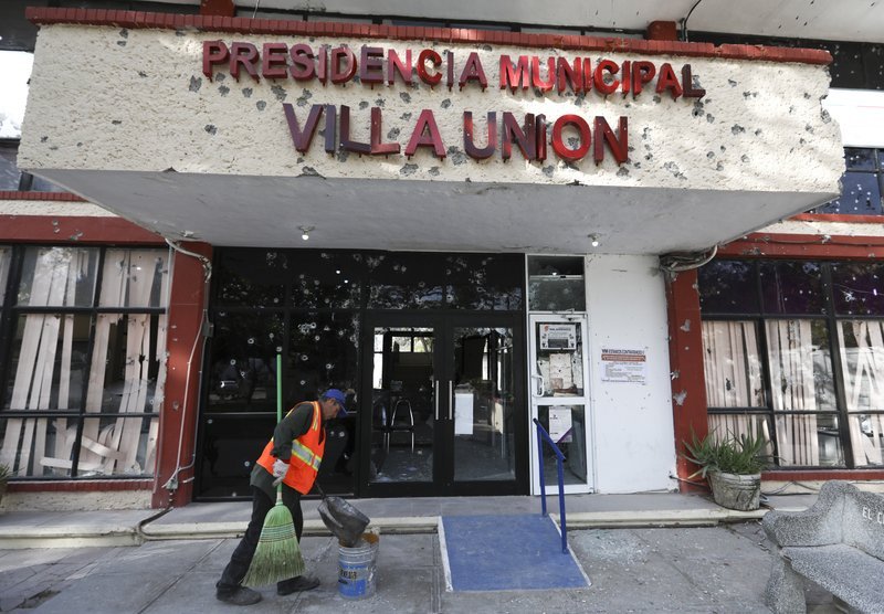 A worker cleans up outside City Hall, riddled with bullet holes, in Villa Union, Mexico, Monday, Dec. 2, 2019. The small town near the U.S.-Mexico border began cleaning up Monday even as fear persisted after 22 people were killed in a weekend gunbattle between a heavily armed drug cartel assault group and security forces. (AP Photo/Eduardo Verdugo)