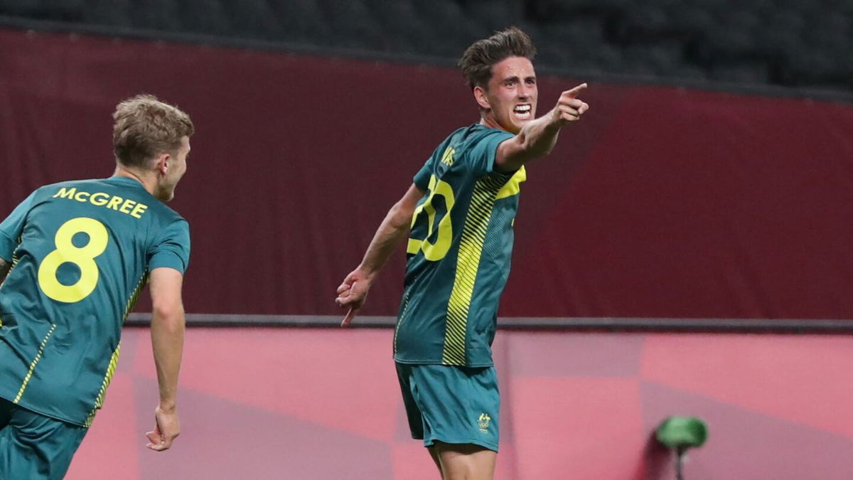 An Australian soccer player points in the direction of the camera