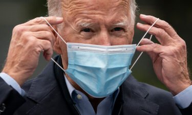 Then-Democratic presidential nominee Joe Biden puts on a face mask while speaking to reporters at a voter mobilization center on October 26