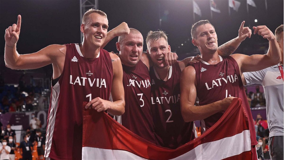 Four Latvian basketball players hold up the Latvian flag in celebration