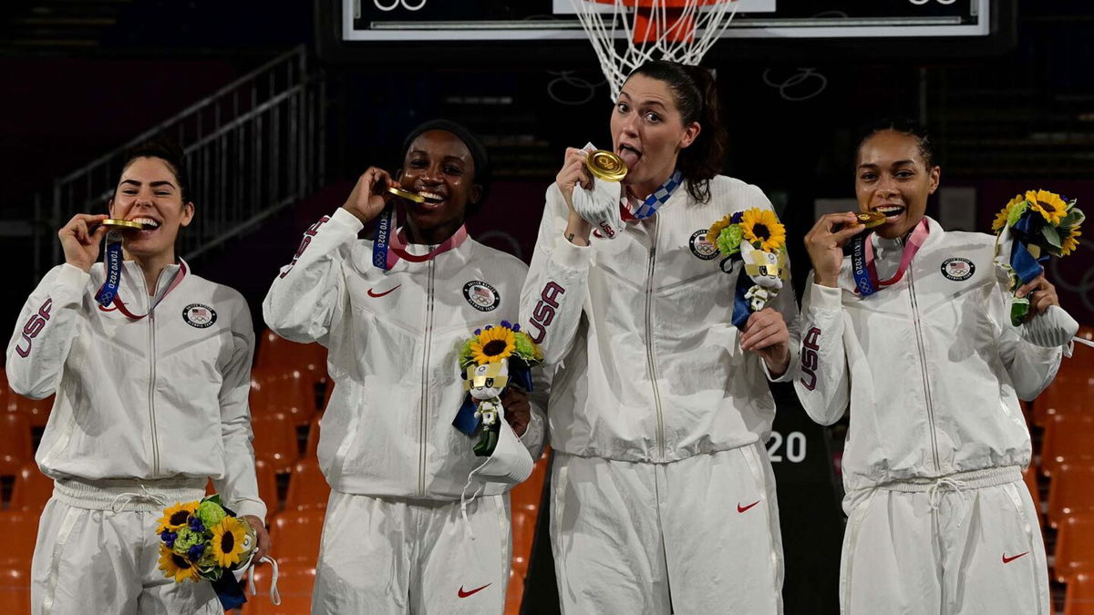 All four members of the U.S. women's 3x3 basketball team bite down on gold medals and hold flowers in their left hands.