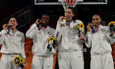 All four members of the U.S. women's 3x3 basketball team bite down on gold medals and hold flowers in their left hands.