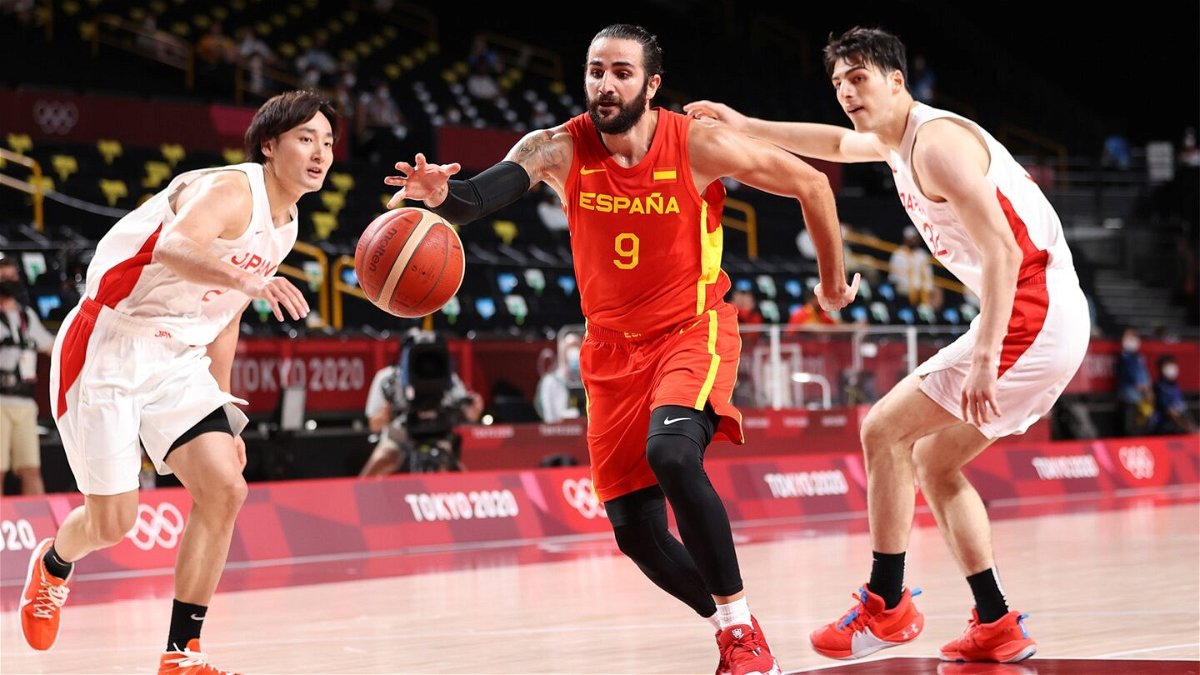 A Spanish basketball player dribbles the ball as two Japanese players chase after him on either side