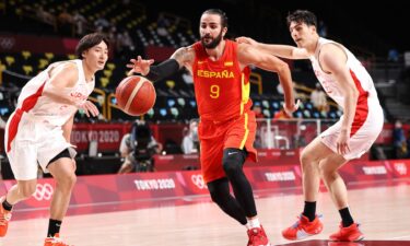 A Spanish basketball player dribbles the ball as two Japanese players chase after him on either side