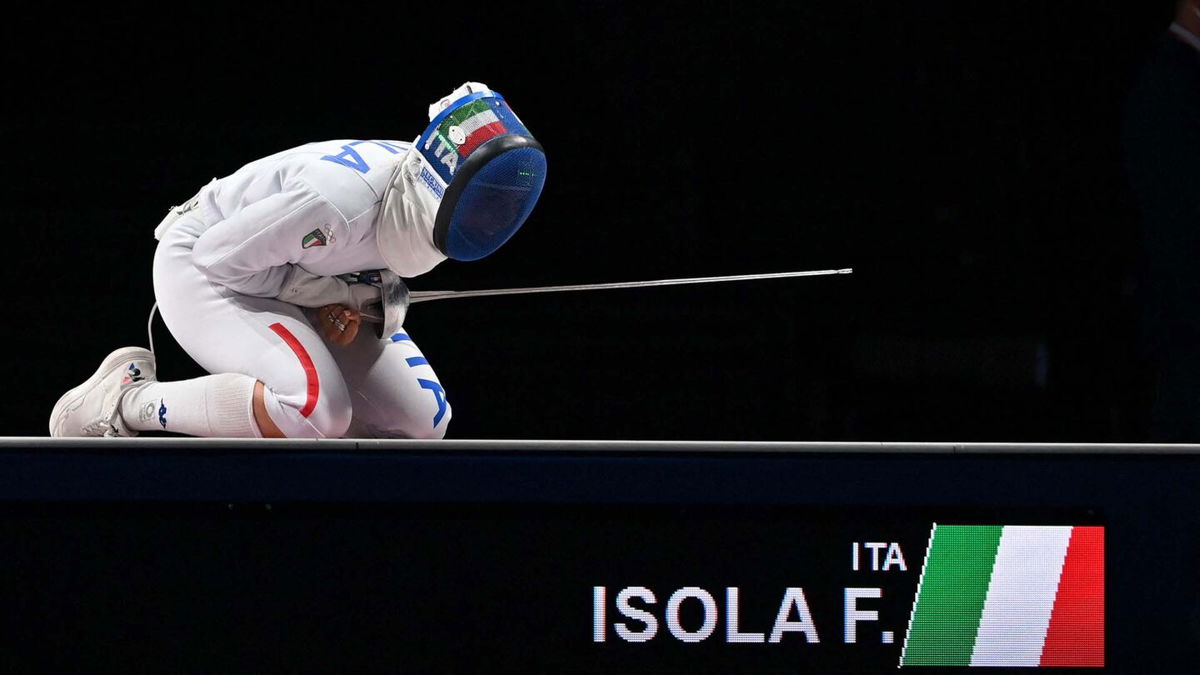 Frederica Isola kneels on the ground in full fencing equipment