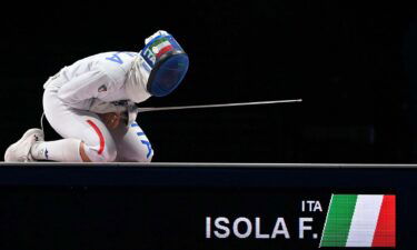 Frederica Isola kneels on the ground in full fencing equipment