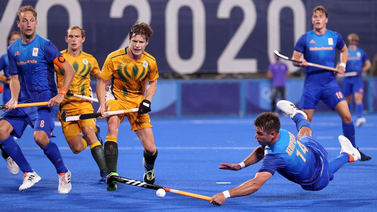 A player in a blue jersey falls to the ground as he reaches towards the ball while other  players look on