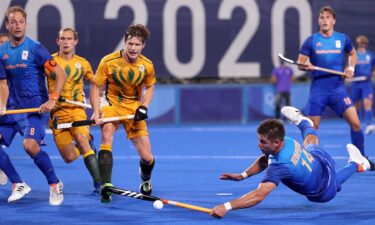 A player in a blue jersey falls to the ground as he reaches towards the ball while other  players look on