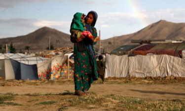 An internally displaced Afghan girl carries a child near their shelter at a camp on the outskirts of Kabul
