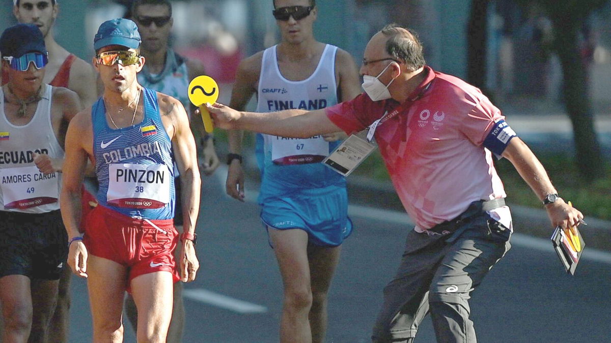 An official (right) holds a yellow sign out at a man racewalking