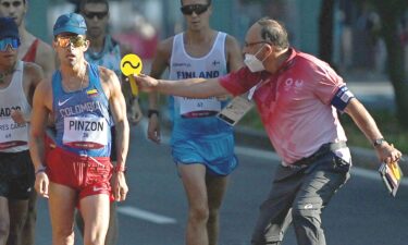 An official (right) holds a yellow sign out at a man racewalking