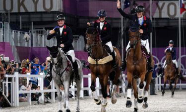 Three people wave and hold medals up as they ride horses