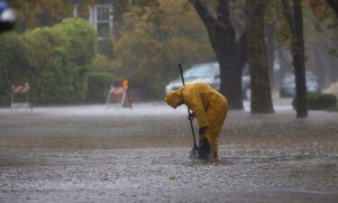 A worker tries to clear a drain in a flooded street Sunday in San Rafael