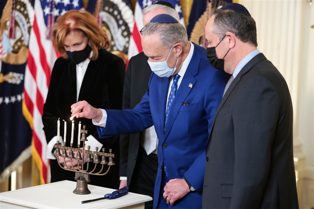 <i>Oliver Contreras/Sipa USA/AP</i><br/>Senate Majority Leader Chuck Schumer lights a menorah as second gentleman Doug Emhoff looks on during a celebration of Hanukkah in the East Room of the White House on Wednesday