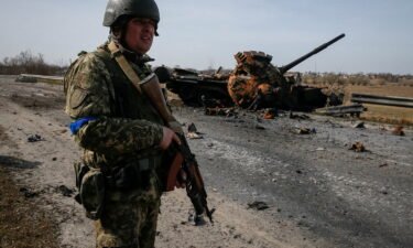 A Ukrainian serviceman stands near the wreck of a Russian tank on the front lines in the Kyiv region