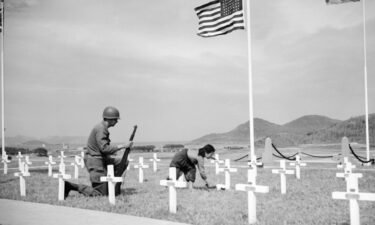 An American corporal watches as a 9-year-old Korean girl places a bouquet of white roses on the grave of one of his fallen comrades at a UN memorial near Busan