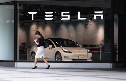 A woman walks past the front window of a Tesla Store in Shinjuku