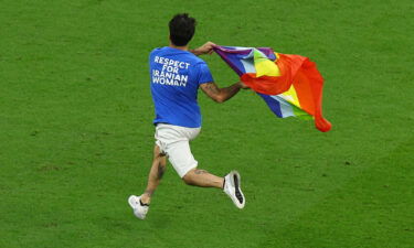 A pitch invader runs onto the pitch wearing a t-shirt with a message saying: 'Respect for Iranian Woman' on the back and holding a rainbow flag.