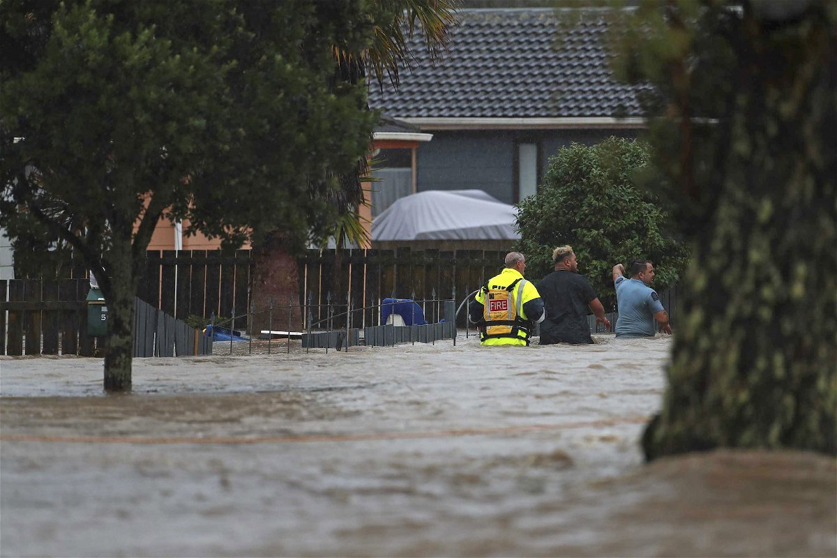 Emergency workers and a man wade through flood waters in Auckland