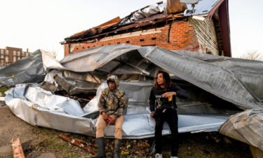 Cordel Tyus and Devo McGraw sit on roofing that blew off of an industrial building and wrapped around their house Thursday after a tornado ripped through Selma