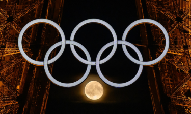 The moon is pictured through the Olympic rings displayed on the Eiffel tower