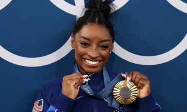 Simone Biles poses with her all-around Olympic gold medal and goat charm necklace at the 2024 Paris Olympics.