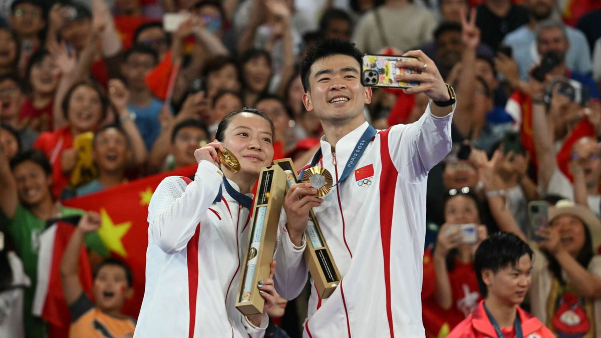 China's Gold medalists Zheng Siwei (R) and Huang Ya Qiong pose for a selfie on the podium at the mixed doubles badminton medal ceremony during the Paris 2024 Olympics at Porte de la Chapelle Arena in Paris on August 2