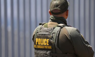 A US Customs and Border Protection Border Patrol agent stands in front of the US-Mexico border wall in Imperial Beach